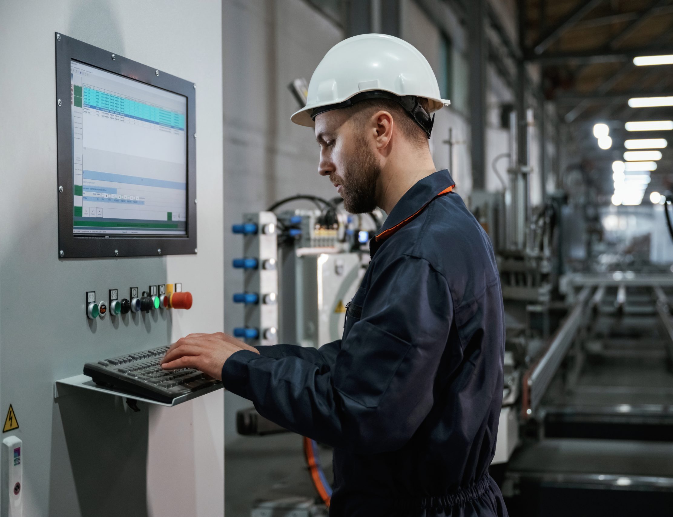 Adjusting settings of machine, operating. Factory worker is indoors with hard hat